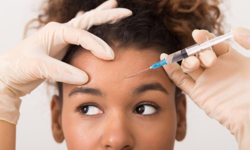Cosmetic procedures. African-american woman getting botox injection in forehead